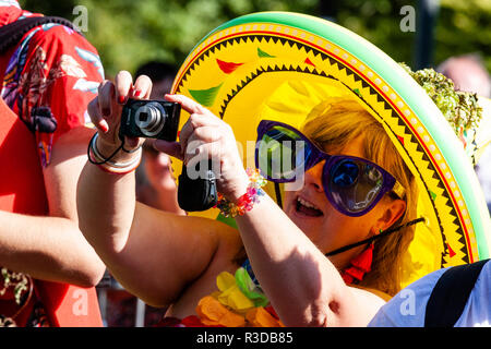 Faversham Hop Festival 2018. Mature woman in audience wearing inflatable yellow Mexican sombrero, and over large sunglasses, taking photograph Stock Photo