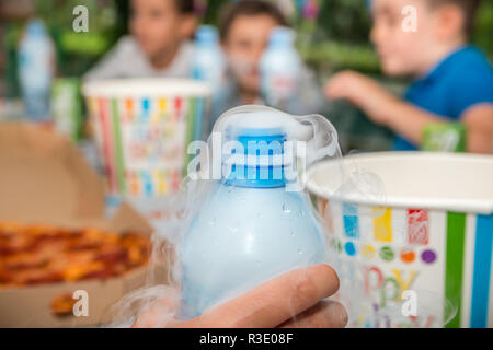 Smoke effect coming out from plastic water bottle in hand on birthday party blurred background. Close up. Stock Photo