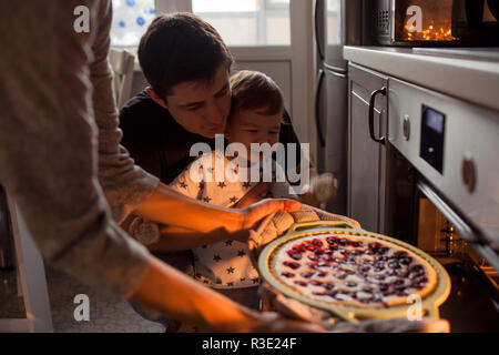 young multiethnic family making a cake together. Mom dad and son pull the cake out of the oven Stock Photo