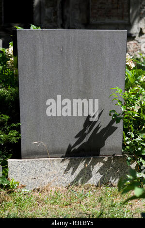 Austere headstone in a cemetery in Berlin, Germany with bright sunlight and shadows from a plant on the stone and no name engraved Stock Photo