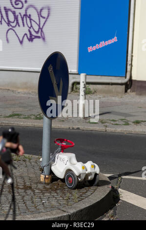 A children's white plastic automobile chained to a signpost on the street in Berlin, Germany with graffiti on the walls in the background Stock Photo