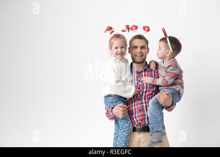 Father holds children in his arms on a white background. Happy family in funny Christmas headbands. Stock Photo