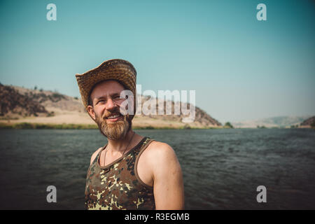 Candid photograph of man in his thirties smiling and looking joyful at camera, standing next to the river. The air is smokey from forest fires. Stock Photo