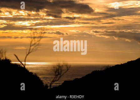 Beautiful sunset over the water with mountain silhouettes at  Waitakere Ranges, West Auckland, New Zealand Stock Photo