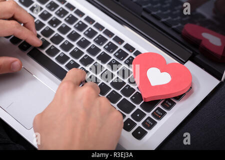 Person's Hand Typing On Laptop Keypad With Red Heart Stock Photo