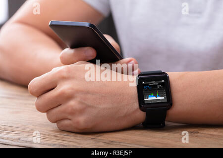 Man's Hand With Mobile And Smartwatch Showing Heartbeat Rate Over Wooden Desk Stock Photo