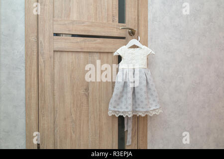 Beautiful festive baby dress hanging on door handle near grey wall. Preparing for the holiday. Waiting for birthday or new year Christmas celebration. Stock Photo