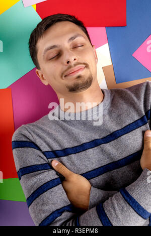 happy young man lying on multicolored paper sheets Stock Photo