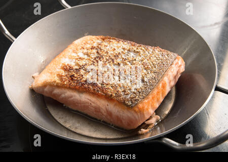 fresh salmon fillet with crispy crust is fried in an iron pan on the stove, selected focus, narrow depth of field Stock Photo
