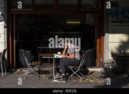 A man reads at a table outside a restaurant in Berlin, Germany Stock Photo