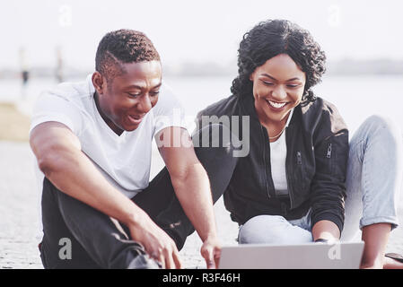 Two happy friends of students or business partners are sitting outdoors and enjoying a laptop Stock Photo