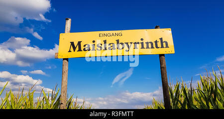Corn Maze is a maze cut from a corn field. Maize labyrinths are popular with tourists and children. Entrance sign in front of blue sky with lettering  Stock Photo