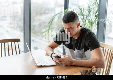Freelancer work on netbook in modern coworking. Young man Typing on a smartphone,. Programmer at remote job. Successful people, businessman in comfortable cafe. High large Windows Stock Photo