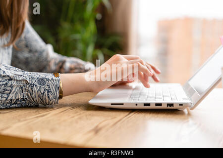 Young woman Typing on the keyboard, chatting, maintains a blog. Freelancer work in modern coworking. Successful people, businessman in comfortable cafe . Reading text during work on netbook. Stock Photo