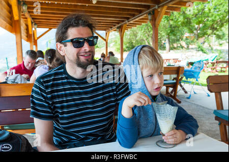 Four year old boy sitting next to his father and eating ice cream in a restaurant in Montenegro Stock Photo