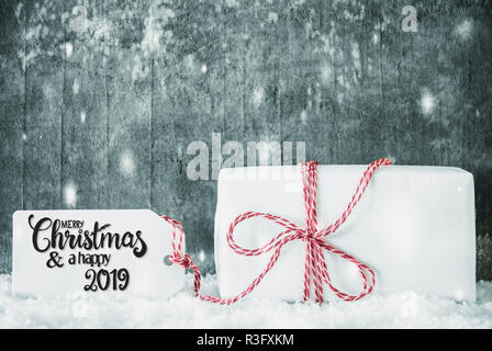 Label With English Calligraphy Merry Christmas And A Happy 2019. One White Gift With Red Ribbn. Grungy Cement Background With Snow Stock Photo