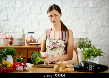 beautiful young woman, brunette cutting broccoli in the kitchen on a table full of organic vegetables
