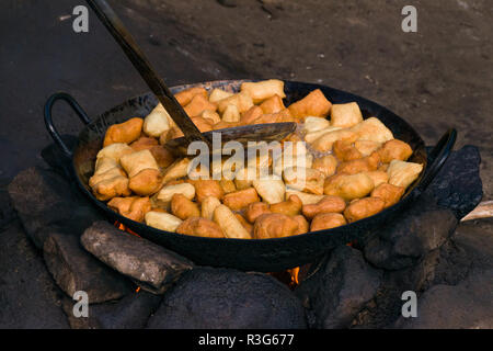 Mandazi, a Swahili fried bread snack, also known as dabo or Dahir, being cooked in a large pan on a stone fire pit in the street, Mathare, Kenya Stock Photo