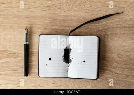 Fountain pen on a notebook. Black ink splash. Wooden table. Copy space. Stock Photo