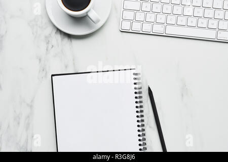 Business composition with white computer keyboard, coffee cup and notebook with pencil on white marble background. Coffee break at the office concept. Stock Photo