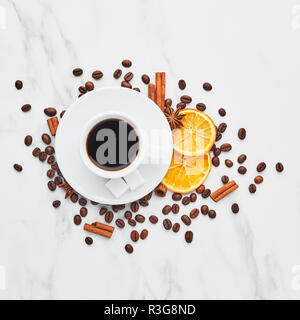 Cup of coffee with beans, chocolate, dried oranges, anis and cinnamon sticks on white marble background. Concept of coffee with different spices. Top  Stock Photo