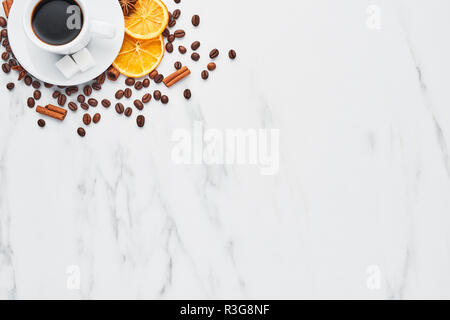 Cup of coffee with beans, chocolate, dried oranges, anis and cinnamon sticks on white marble background. Concept of coffee with different spices. Top  Stock Photo
