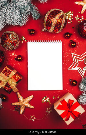Glittering Christmas decorations and white notebook on red background. Flat lay style. Vertical photo. Stock Photo