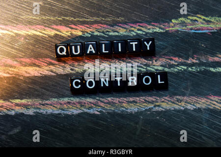 Quality Control on wooden blocks. Cross processed image with blackboard background. Inspiration, education and motivation concepts Stock Photo