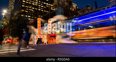Long exposure photo of buses and people crossing an intersection in New York City while steam coming out from the manhole. Stock Photo