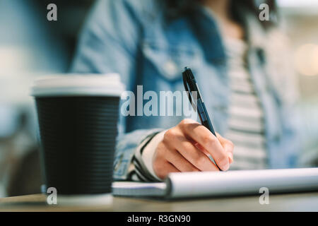 Close up of female student hand writing on notepad with pen. Student making notes in her book. Stock Photo
