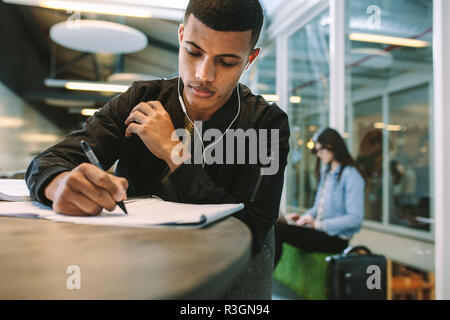 Young man making notes on book. Male student preparing for exams at university library. Stock Photo