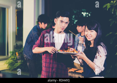 Asian group of friends having outdoor garden barbecue laughing with alcoholic beer drinks on night Stock Photo