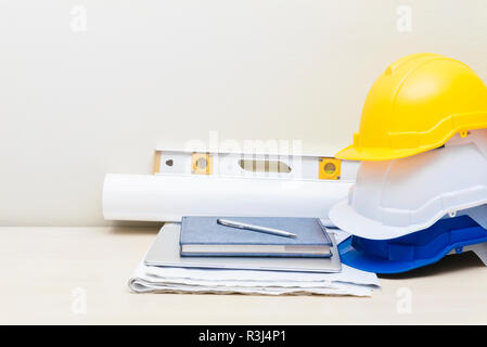 Engineering accessories, helmets, house paper model, business bag, blueprint, on wood table with white concrete wall background. Picture for add text  Stock Photo