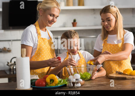 cute happy child with mother and grandmother cooking vegetable salad together in kitchen Stock Photo