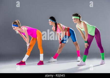 athletic young women in 80s style sportswear smiling at camera on