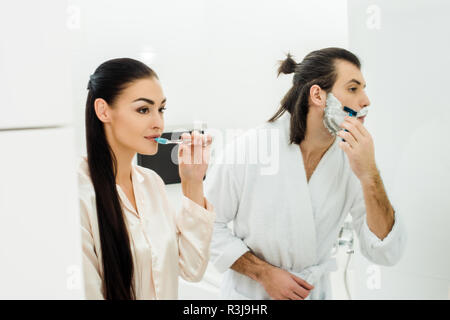 Beautiful woman cleaning teeth while husband shaving beard Stock Photo