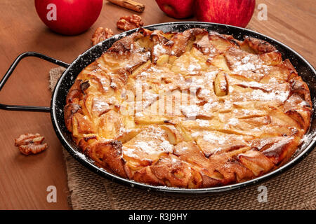 A photo of an apple pie in a pan, on a dark rustic wooden background with apples and walnuts Stock Photo