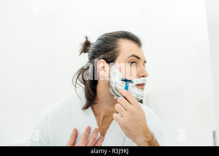 Handsome man in bathrobe shaving in bathroom Stock Photo