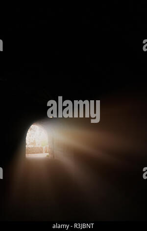 Sunlight and sunrays getting into the long dark tunnel cut through the rock on a sea coast Stock Photo