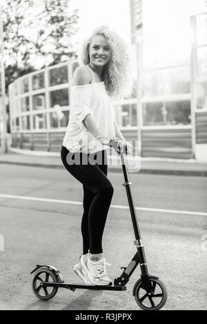 Full-length photo of curly-haired athletic woman kicking on scoo Stock Photo