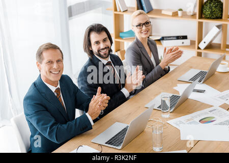 smiling business people clapping hands at meeting in office Stock Photo