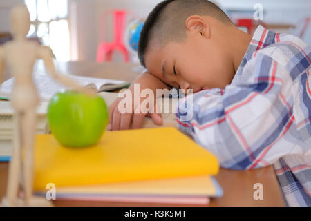 lazy stressed young little asian kid boy  resting sleeping on desk. child fall asleep. children tired from studying in classroom. childhood education Stock Photo