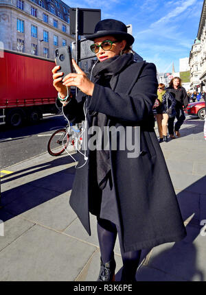 London, England, UK. Woman wearing a hat, filming on her mobile phone while walking Stock Photo