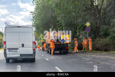 Nyiregyhaza, Hungary, September 06, 2017 Orange car and brigade road repair workers in orange suits on the highway. Asphalt road workers repairs road Stock Photo