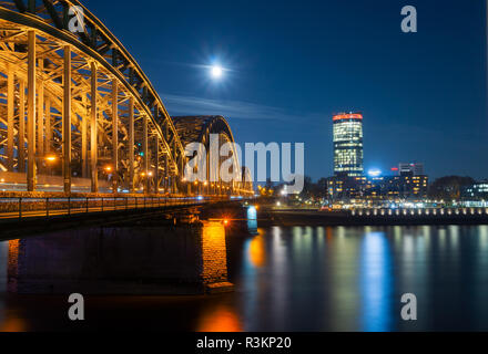 View of the Hohenzollernbridge, the Cologne Triangle, the Hyatt Regency and a beautiful bright Full Moon over the River Rhine at Night in Germany Colo Stock Photo