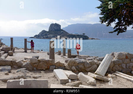 Tourists exploring the ruins of the Basilica of Ayious Stefanos at Kamari on the Greek island of Kos. The island of Kastri is also seen in the bay. Stock Photo