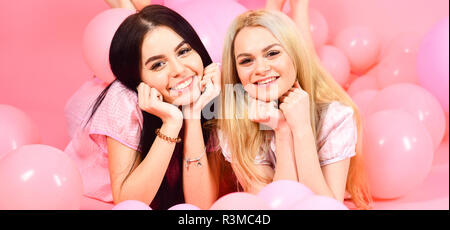 Gossip concept. Blonde and brunette on smiling faces have fun at domestic bedroom party. Sisters or best friends in pajamas at girlish pajamas party.  Stock Photo