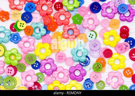 A collection of colourful sewing buttons and beads on a painted white wood background