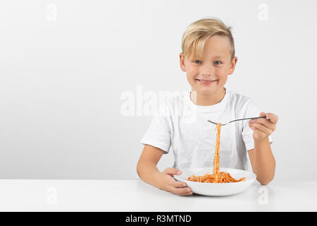 little blond boy in front of white background eats spaghetti and smiles Stock Photo