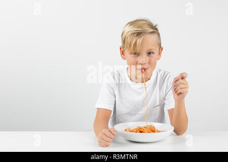 little blond boy in front of white background eats spaghetti and smiles Stock Photo